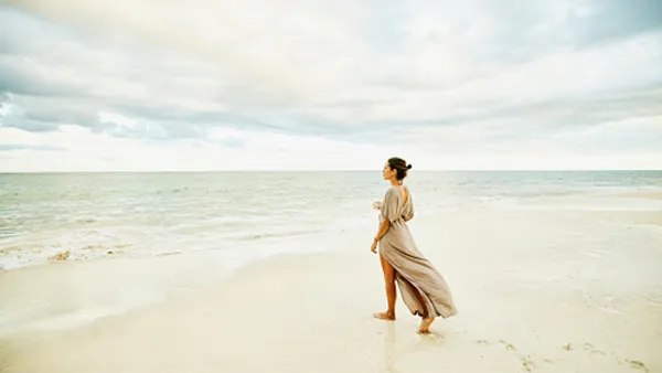 woman walking on beach in beige dress