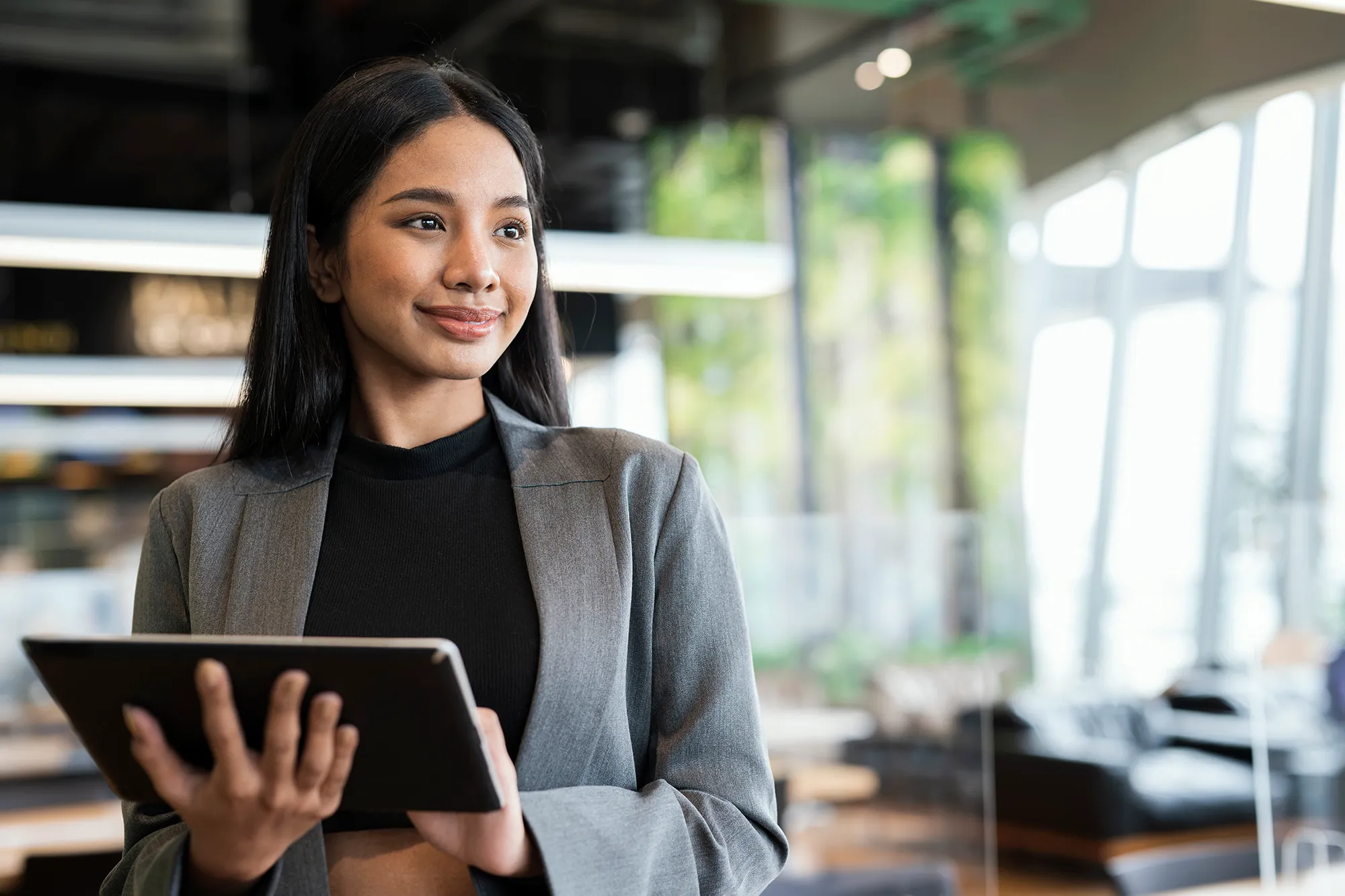 Businesswomen using a tablet while standing and looking away in a financial business office.