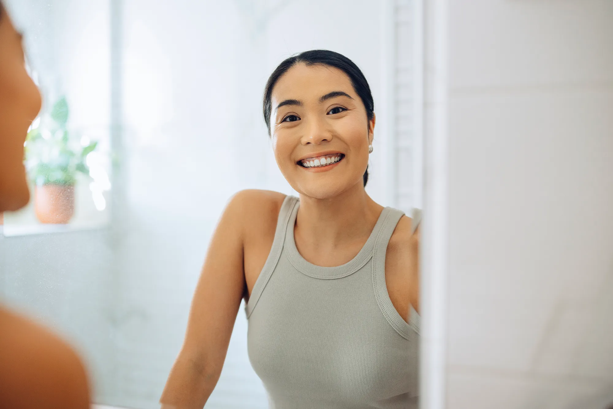 Cheerful Woman standing at her sink in the bathroom, looking at herself in the mirror.