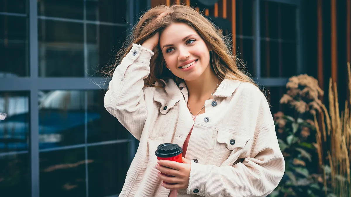 Blonde girl student girl smiles and walks around the city and stands on the background of a cafe, restaurant. Portrait of a girl in the city