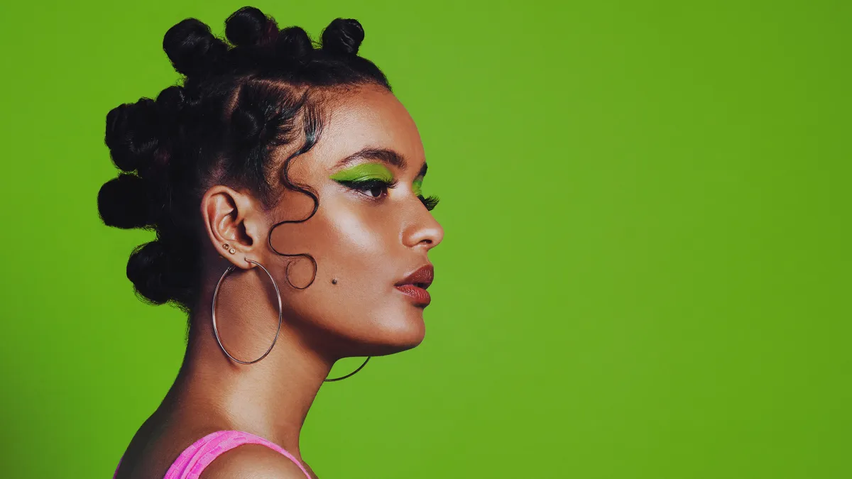 Shot of a woman posing against a green background with her bantu knots