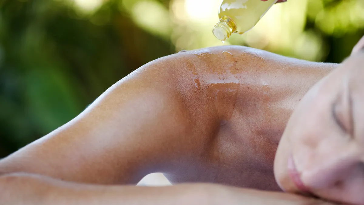 Young woman relaxing, massage oil being poured on back, close-up