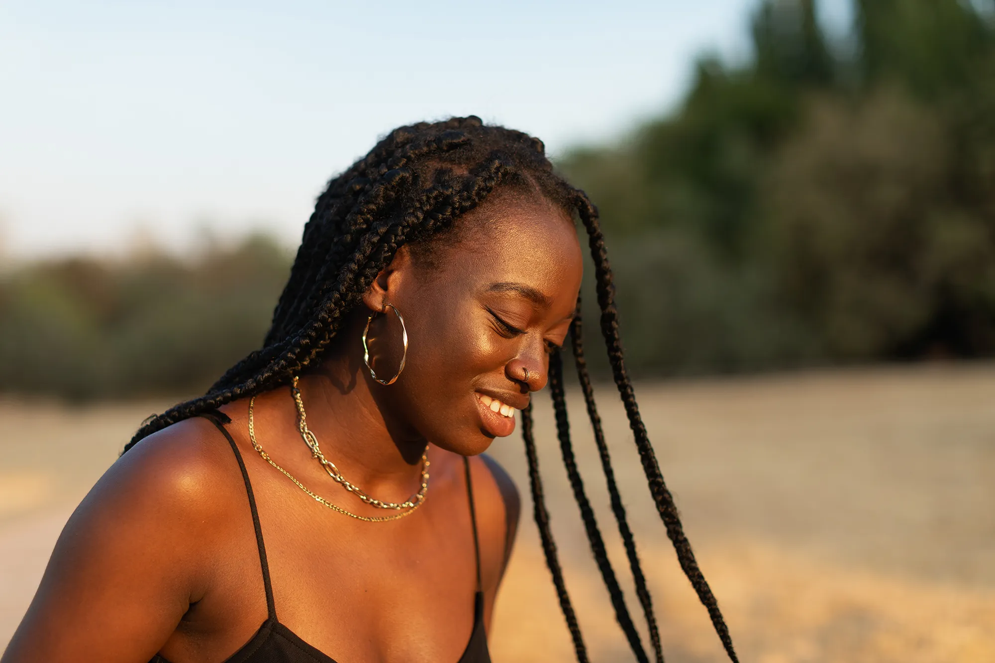 Close-up portrait of a young woman looking down while her braids move with inertia in the park at sunset