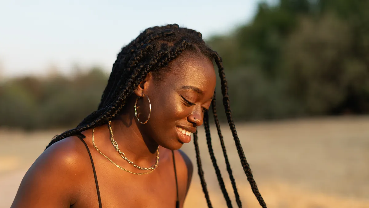 Close-up portrait of a young woman looking down while her braids move with inertia in the park at sunset