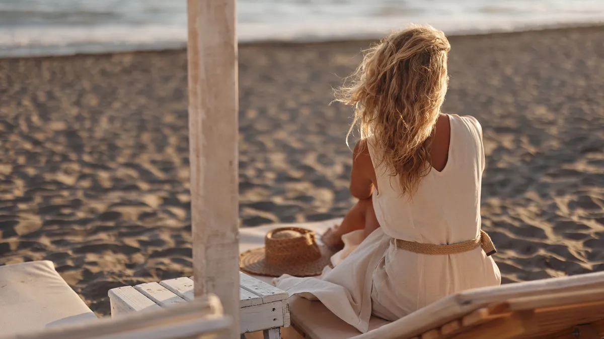 Rear view of carefree woman relaxing on a deck chair during summer day on the beach. Copy space.