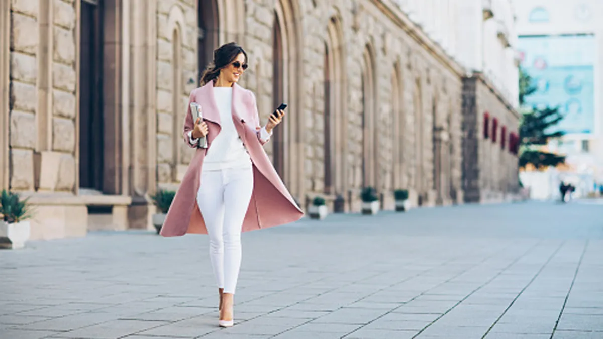 woman walking on street wearing pink blazer and white pants