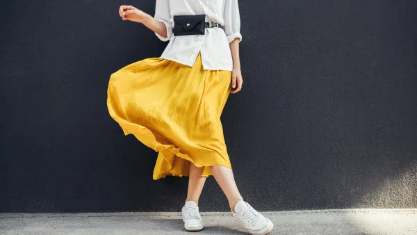 Horizontal cropped image of stylish slim woman in beautiful yellow skirt. Caucasian female fashion model standing over gray wall background outdoor with copy space.