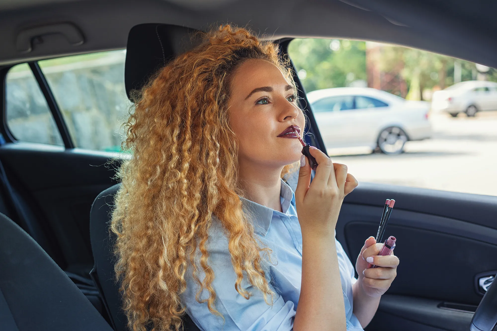 Beautiful woman putting on lip gloss in car