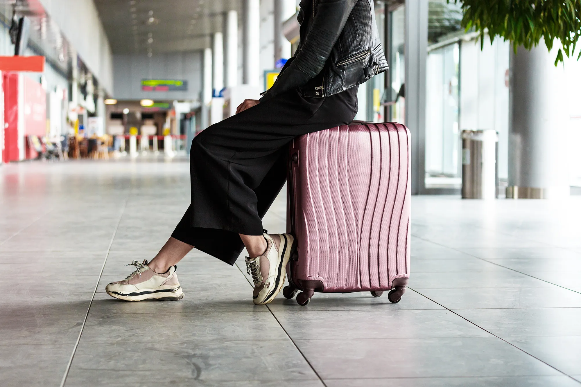 Young woman sitting on luggage in airport terminal.