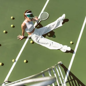 high angle view of beautiful woman in stylish white clothing sitting on tennis court with balls and racket around
