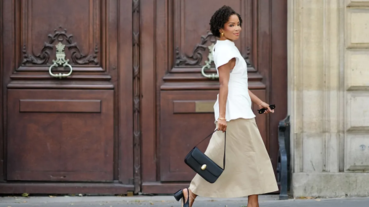 woman wearing white top, beige skirt and black bag