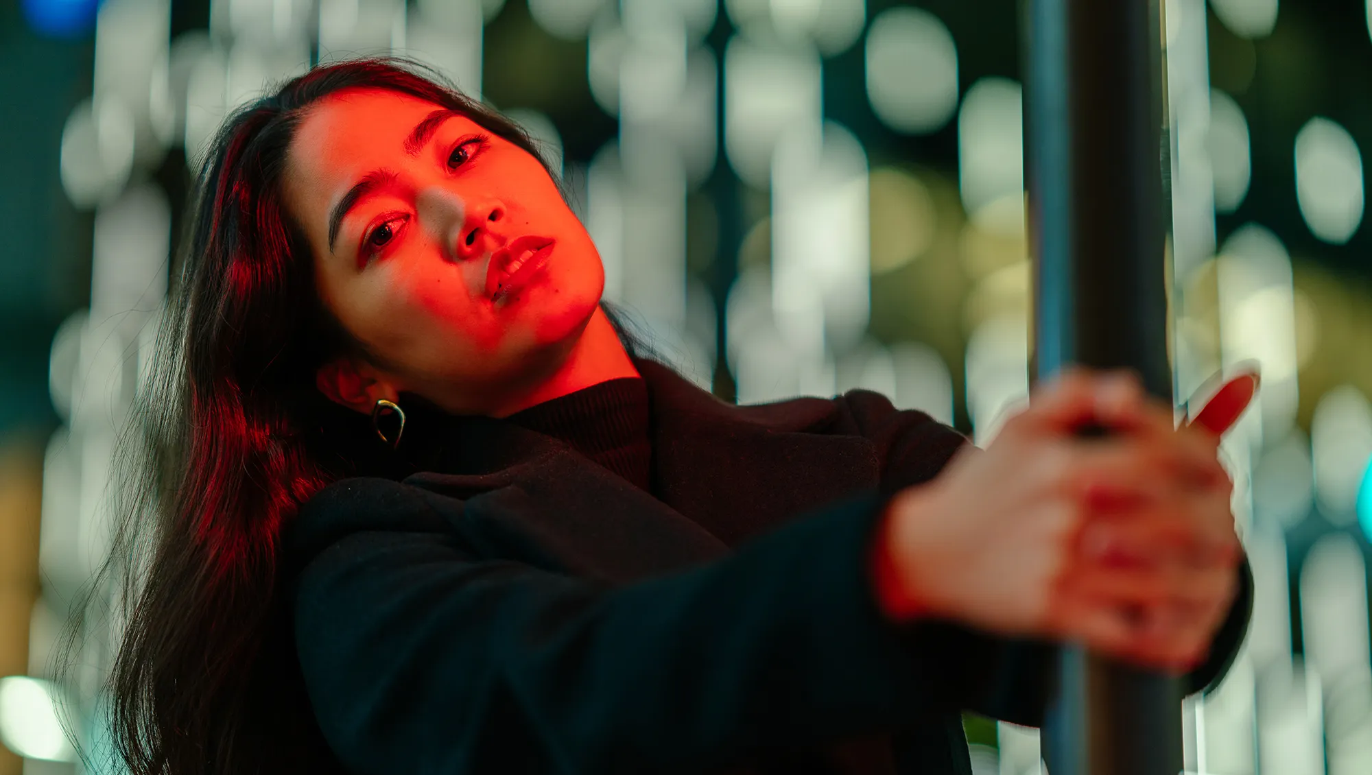 A portrait of a young woman lit by neon colored light in the city at night.