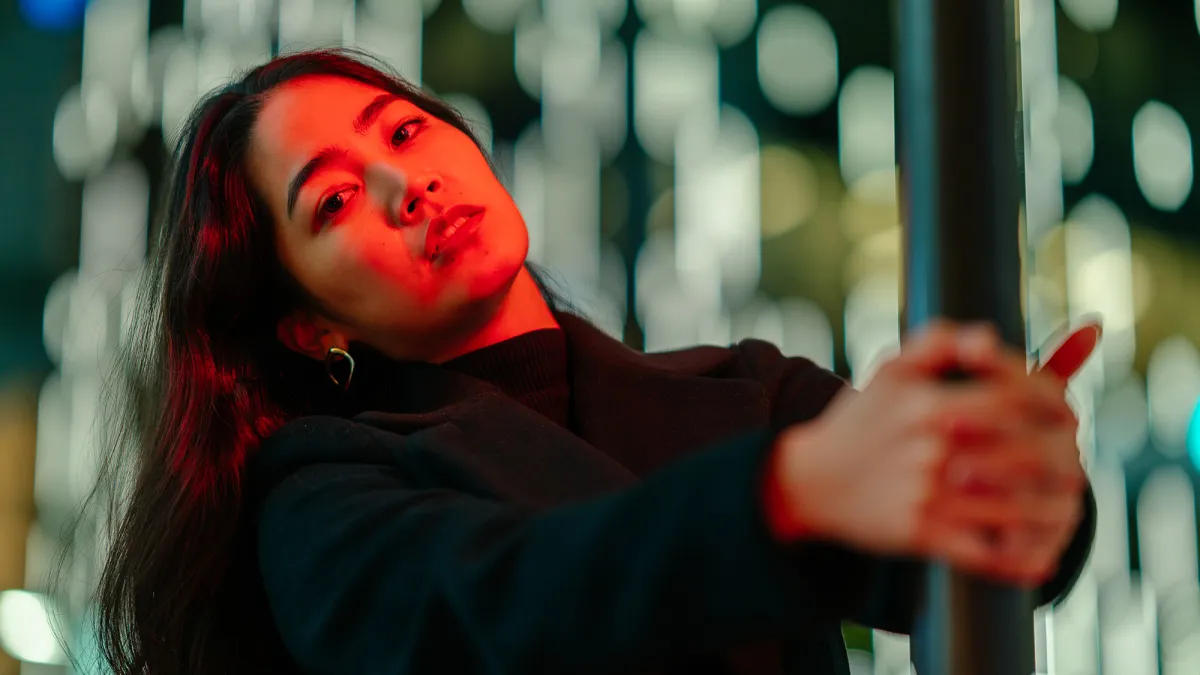 A portrait of a young woman lit by neon colored light in the city at night.