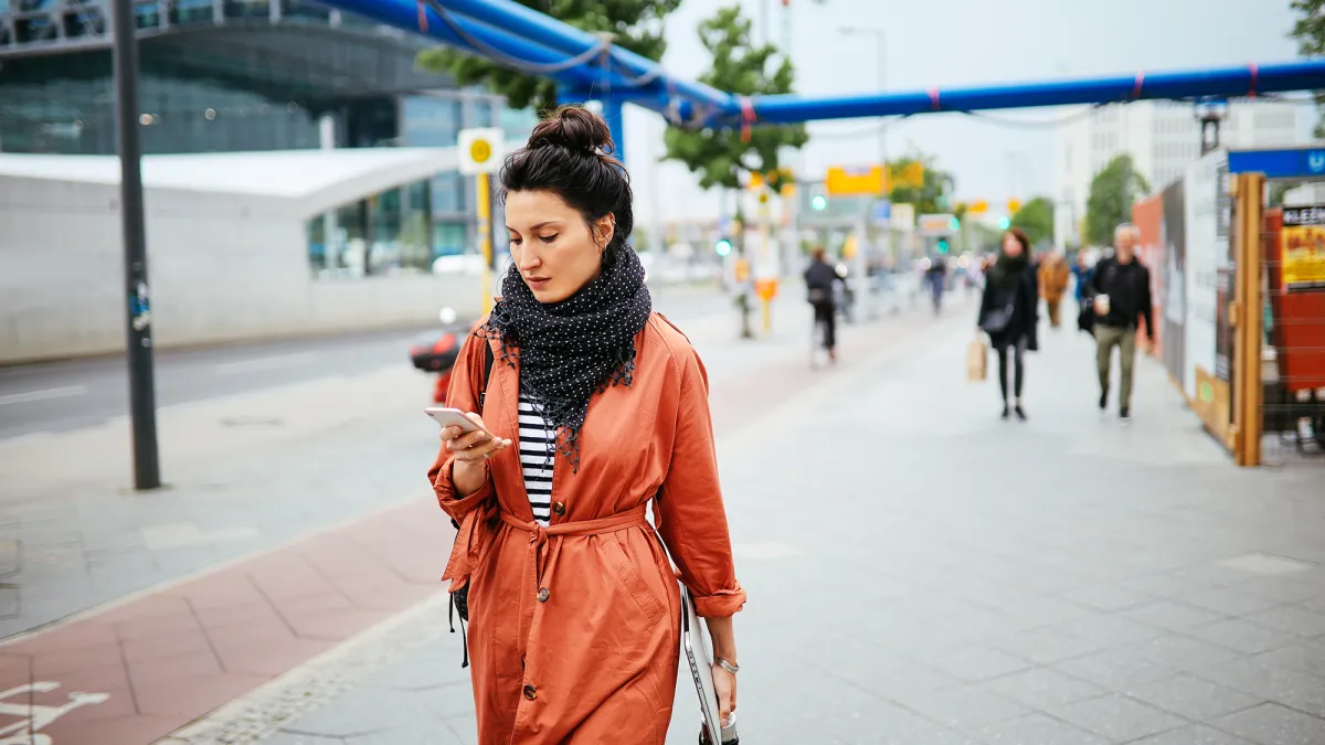 Young commuter woman, walking in Berlin, carrying her laptop, checking apps on the mobile phone.