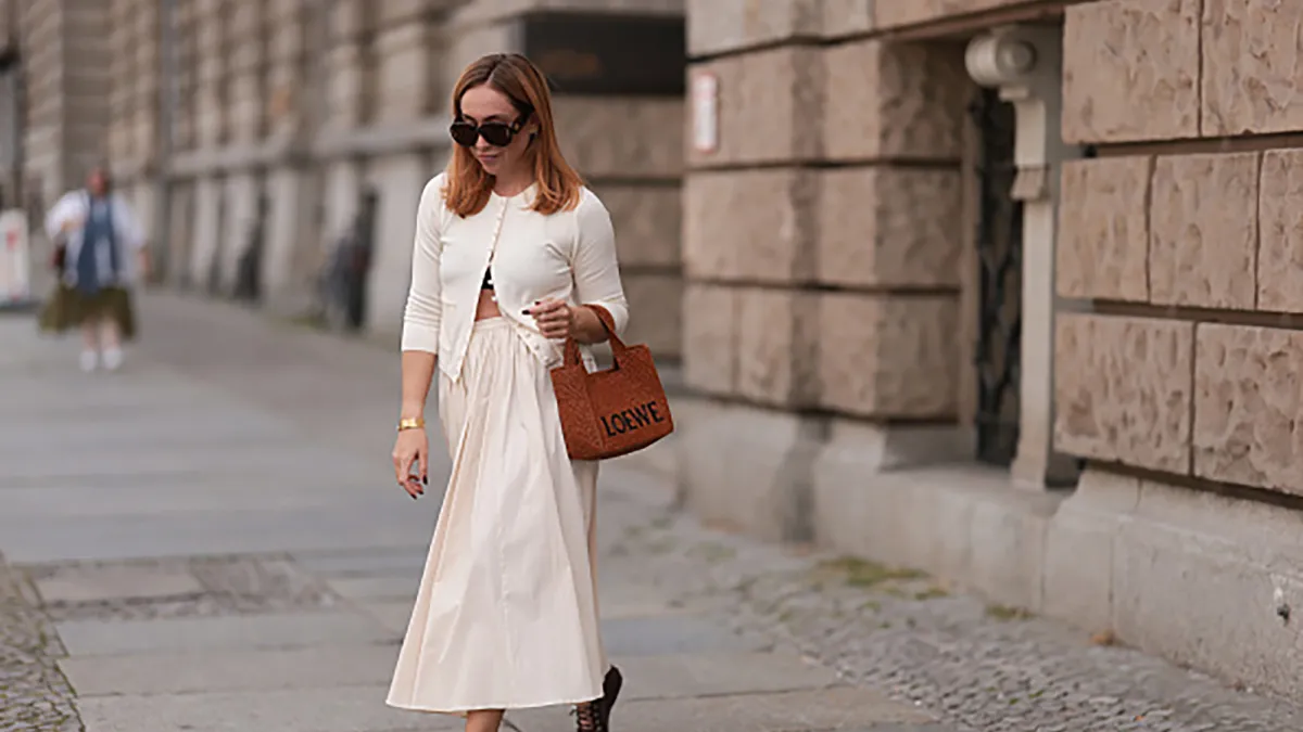 BERLIN, GERMANY - AUGUST 22: Sonia Lyson seen wearing Loewe brown sunglasses, Zara creamy white cotton buttoned cardigan, matching Zara creamy white long pleated skirt, Loewe cognac brown logo raffia bag and Zara burgundy leather ballerinas, on August 22, 2024 in Berlin, Germany. (Photo by Jeremy Moeller/Getty Images)
