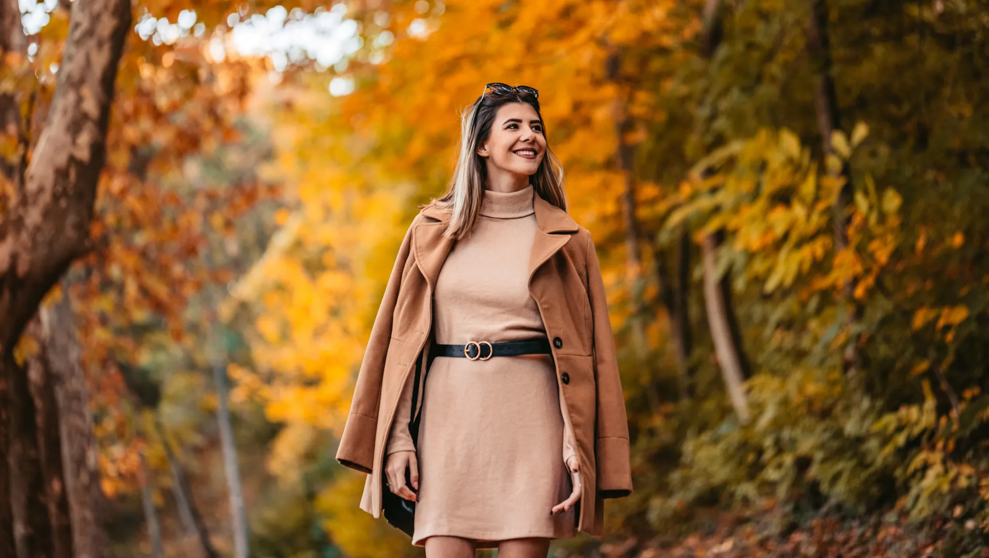 a woman walking through a park in the fall