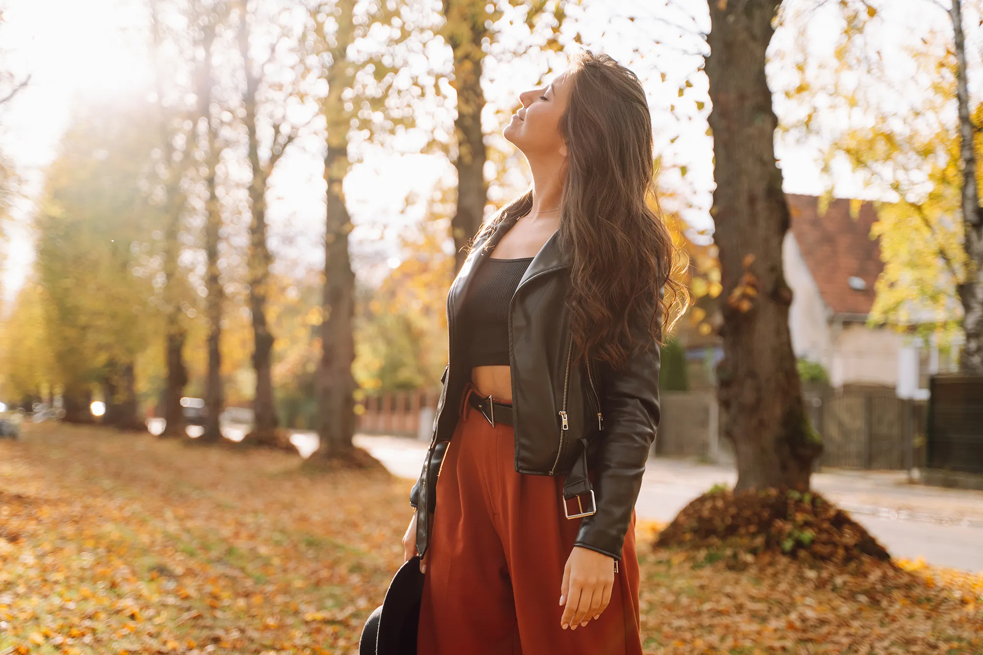 Woman standing in autumn park, breathing deeply and smiling with closed eyes