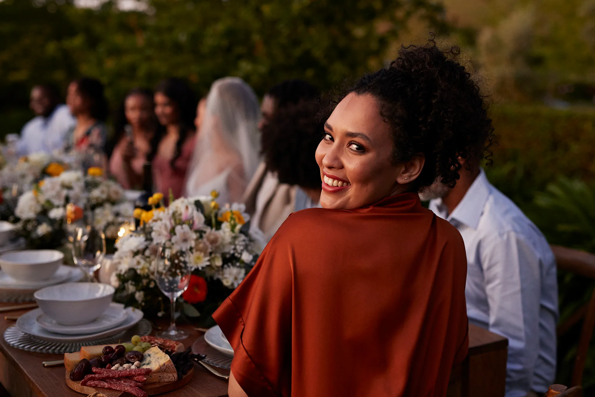 Rear view portrait of happy young woman guest looking back while sitting at dining table during wedding