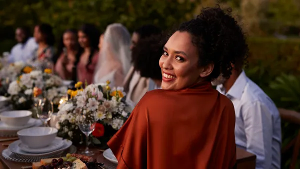 Rear view portrait of happy young woman guest looking back while sitting at dining table during wedding