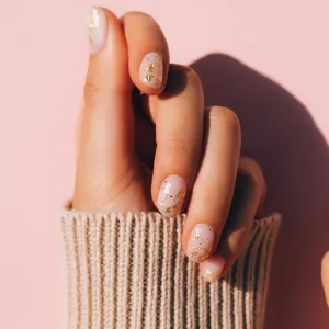 Glowing hands in sweater with knitted sleeves and with nude color manicure with gold particles on pink table. Trendy colors of the year