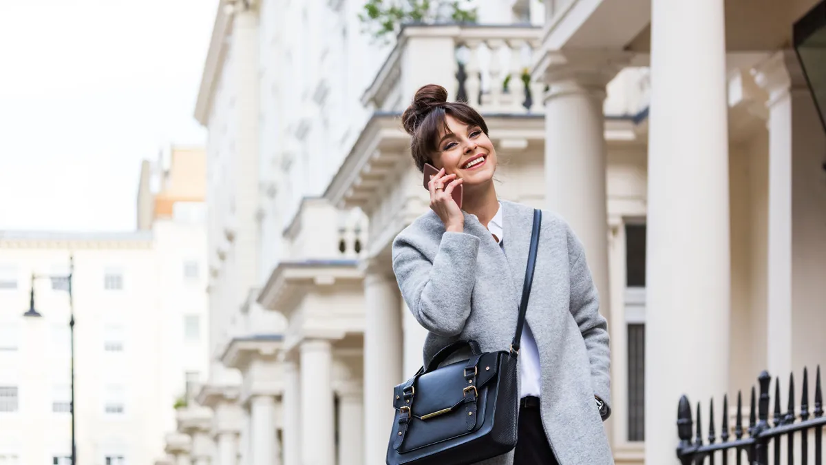 Elegant beautiful woman talking on phone in front of city houses