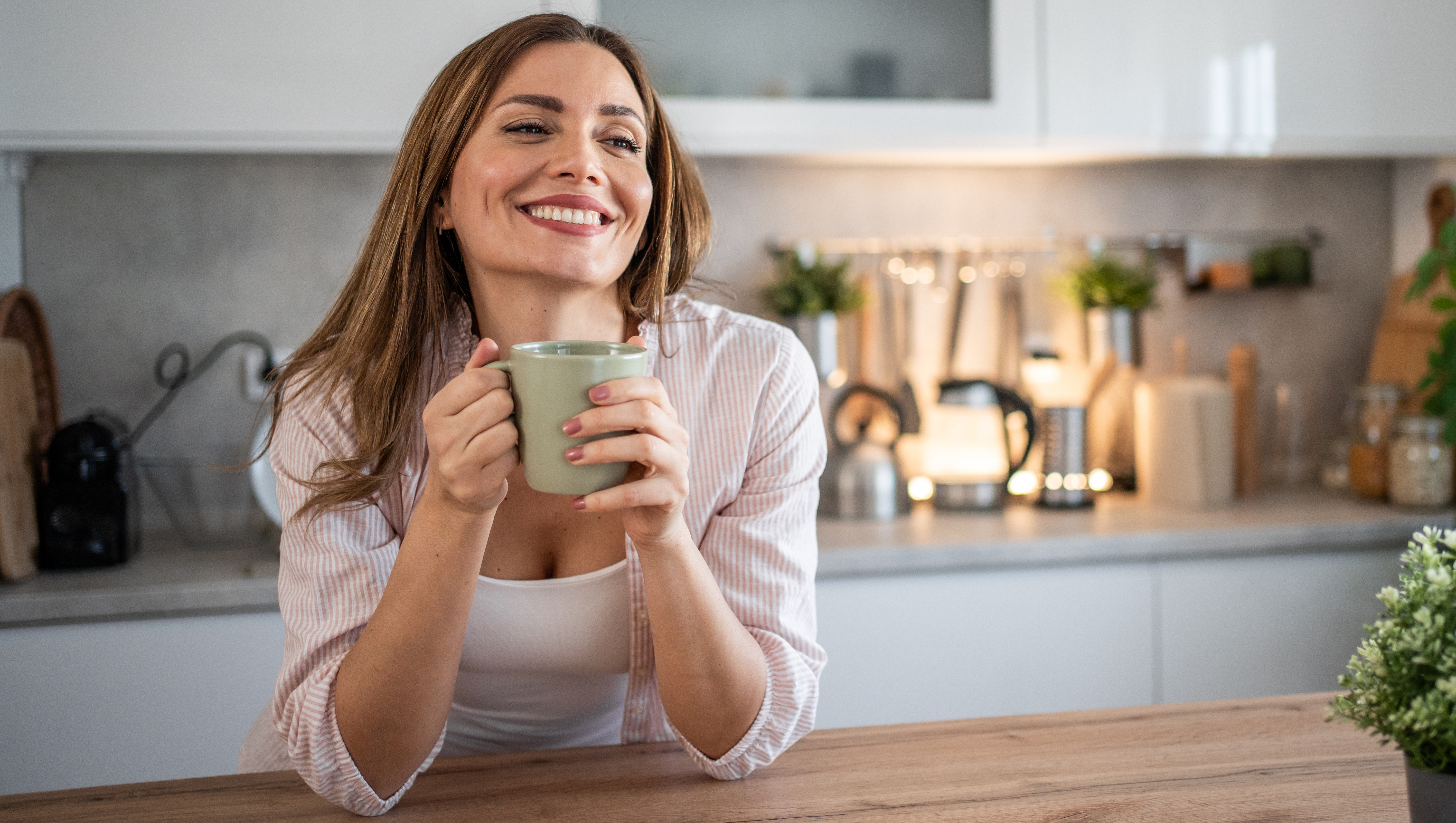 A young woman enjoys her kitchen, dressed in pajamas, drinking her morning coffee