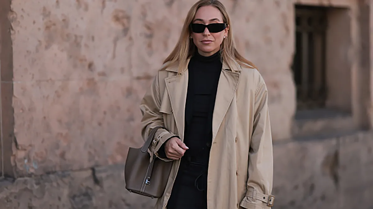 BERLIN, GERMANY - OCTOBER 08: Sonia Lyson is seen wearing black rectangular sunglasses featuring wide temples with triangular logo embellishment from Prada; several earrings and ear studs in silver and gold; an outfit from Levi's consisting of a calf-length beige trench coat with notch lapels and belted cuffs, a black fitted turtleneck, and dark grey wide-legged jeans with a tie belt; and a rectangular brown leather "Picotin" handbag with white decorative seams from Hermès on October 08, 2024, in Berlin, Germany. (Photo by Jeremy Moeller/Getty Images)