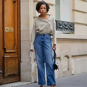 PARIS, FRANCE - MAY 20: Ellie Delphine wears golden earrings, a necklace from Missoma a beige oversized off-shoulder top / shirt from The Frankie Shop, blue wide-leg denim pants / jeans from H&M, a black leather bag from Neous, T sandals / heels shoes from Neous, during a street style fashion photo session, on May 20, 2024 in Paris, France. (Photo by Edward Berthelot/Getty Images)