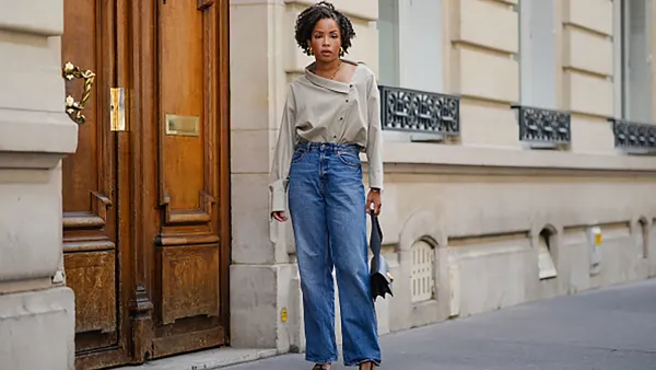 PARIS, FRANCE - MAY 20: Ellie Delphine wears golden earrings, a necklace from Missoma a beige oversized off-shoulder top / shirt from The Frankie Shop, blue wide-leg denim pants / jeans from H&M, a black leather bag from Neous, T sandals / heels shoes from Neous, during a street style fashion photo session, on May 20, 2024 in Paris, France. (Photo by Edward Berthelot/Getty Images)