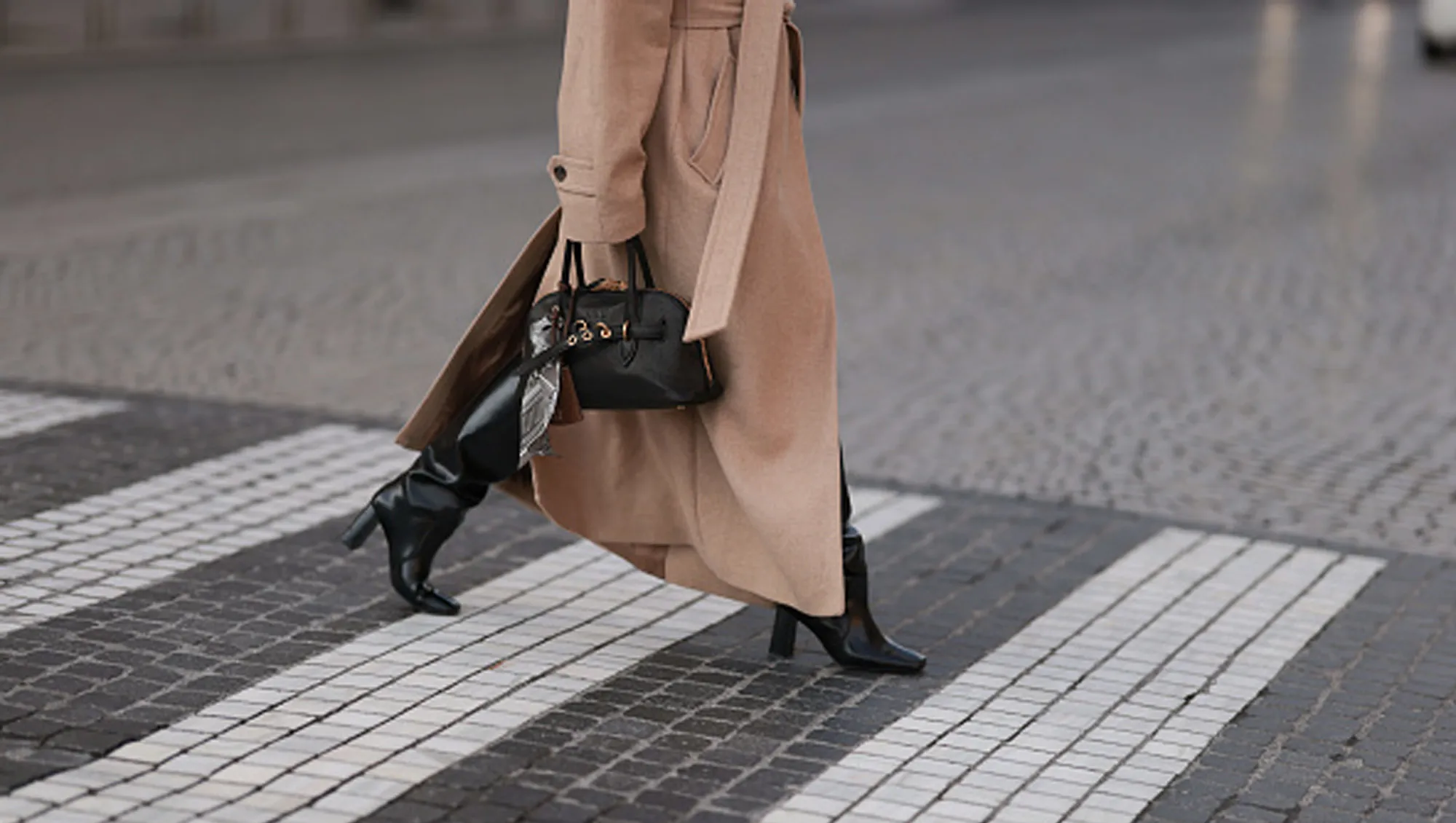 woman wearing a beige coat with boots and bag on street