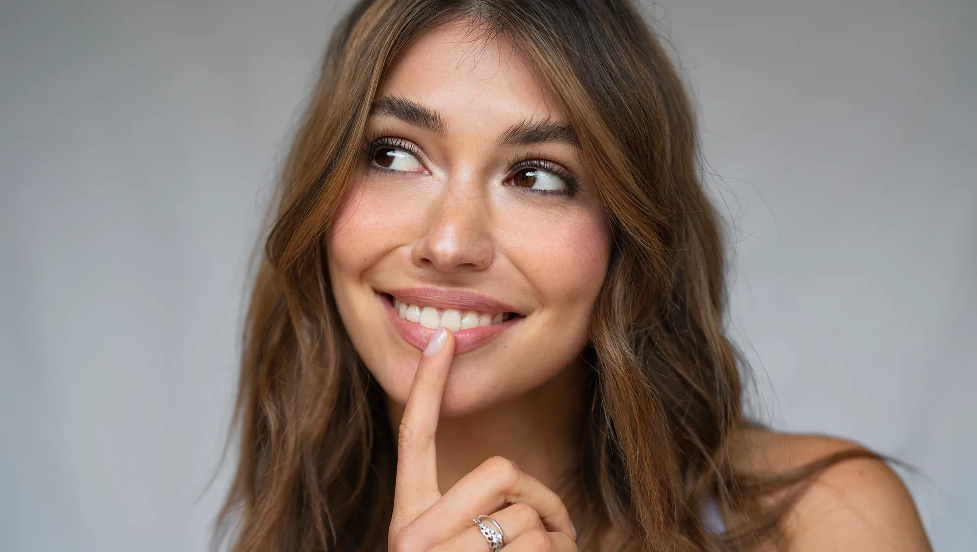 Portrait of a young brunette woman smiling, with index finger on lower lip