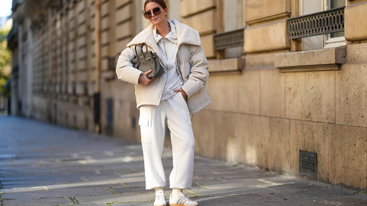 woman wearing beige coat, sweatpants, sneakers and a purse