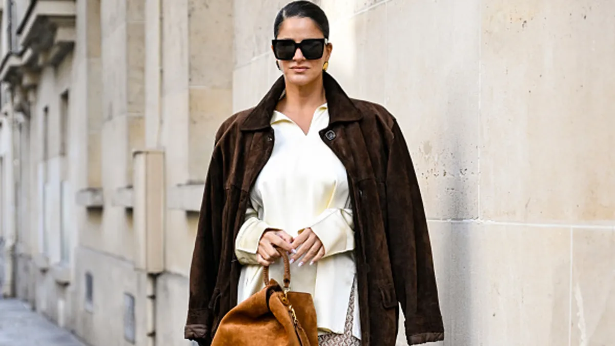 fashionable woman wearing brown suede jacket, cream top and brown suede bag