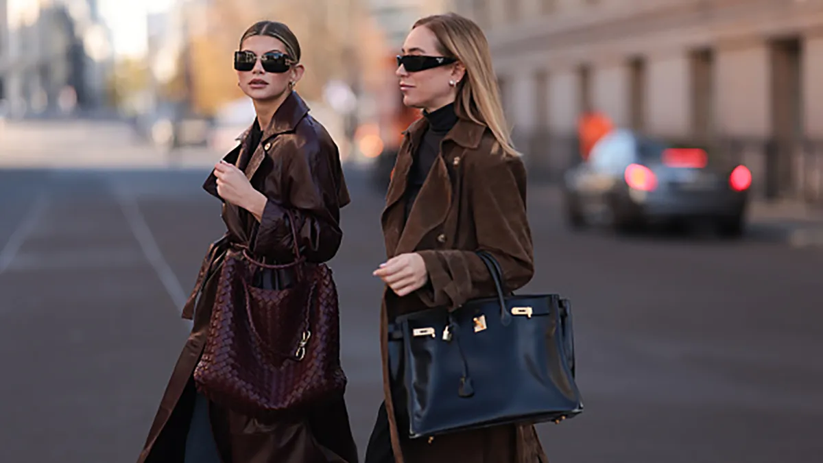 BERLIN, GERMANY - OCTOBER 23: Sophia Geiss (left) is seen wearing rimless oversized sunglasses with brown curved lenses with logo-embellishment, slim gold metal temples paired with the matching gold metal nose bridge from Miu Miu; two different-sized gold hoop earrings; a silver nose ring; an ankle-length burgundy leather coat with large notch lapels, belted cuffs, and a tie belt from Ducie London; a black knit pullover with round neckline underneath; wide-legged jeans from Closed; and a large “Andiamo“ bag in burgundy woven leather from Bottega Veneta. Next to her, Sonia Lyson (right) is seen wearing black rectangular sunglasses featuring wide temples with triangular logo embellishments from Prada; round diamond stud earrings paired with diamond-studded hoop earrings; an ankle-length brown suede trench coat with large notch lapels, belted cuffs, a double button placket, and a tie belt from Ducie London; a black turtleneck from Levi’s underneath; a large black leather “Birkin“ bag from Hermès; and black wide-legged pants from Massimo Dutti;. They are seen on October 23, 2024 in Berlin, Germany. (Photo by Jeremy Moeller/Getty Images)