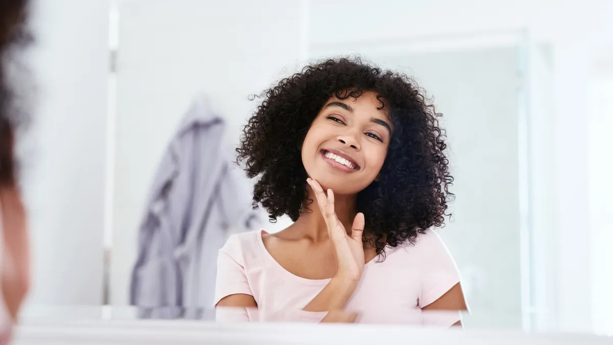 Cropped shot of an attractive young woman smiling while admiring her face in the bathroom mirror at home