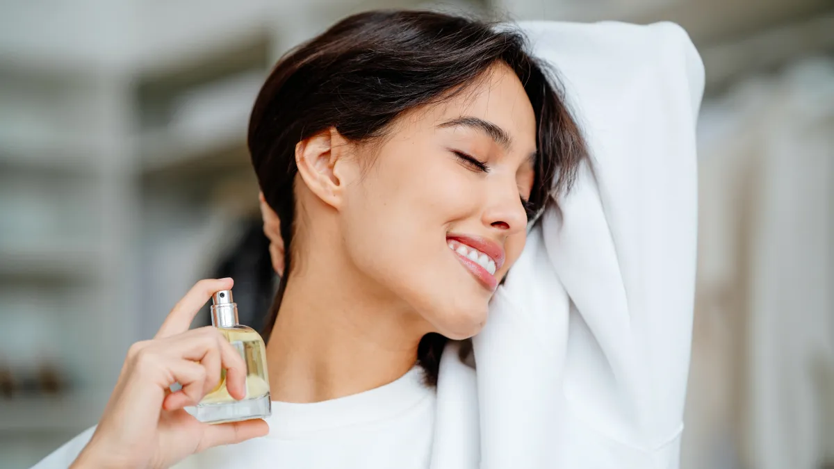 Smiling and joying bob haired woman applying spraying perfume bottle as essential oil on the neck