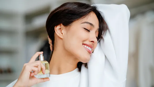 Smiling and joying bob haired woman applying spraying perfume bottle as essential oil on the neck