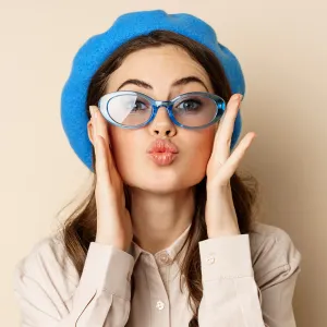 Beautiful stylish woman in sunglasses, blowing air kiss on hands near lips, gazing softly and flirty at camera, posing against beige background.