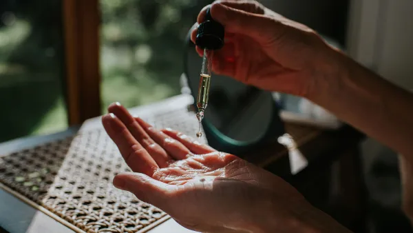 A woman in a bath robe spends some time moisturising her hands. She drops some cosmetic oil from a pipette onto the palm of her hand.