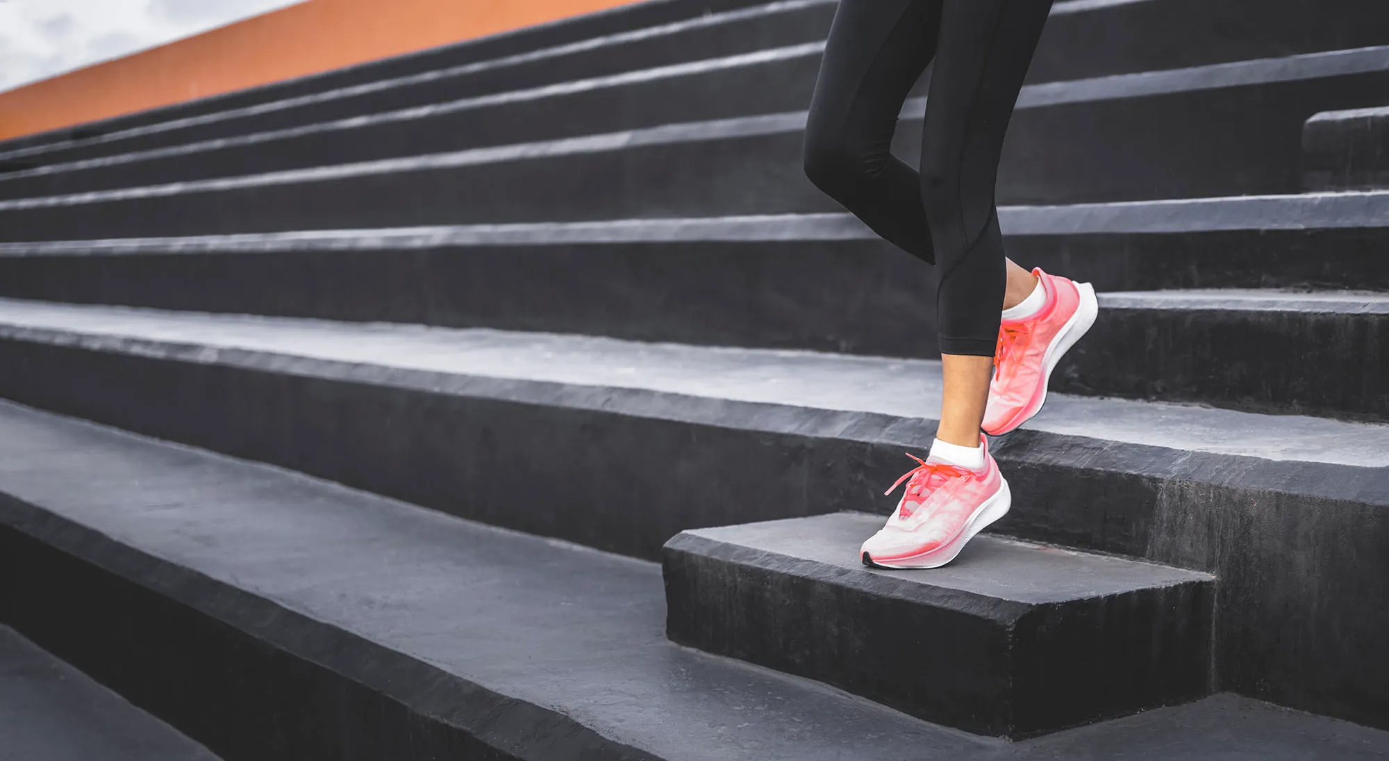 Stairs climbing running woman doing run down steps on staircase. Female runner athlete going down stairs in urban city doing cardio sport workout run outside during summer. Activewear leggings and shoes.