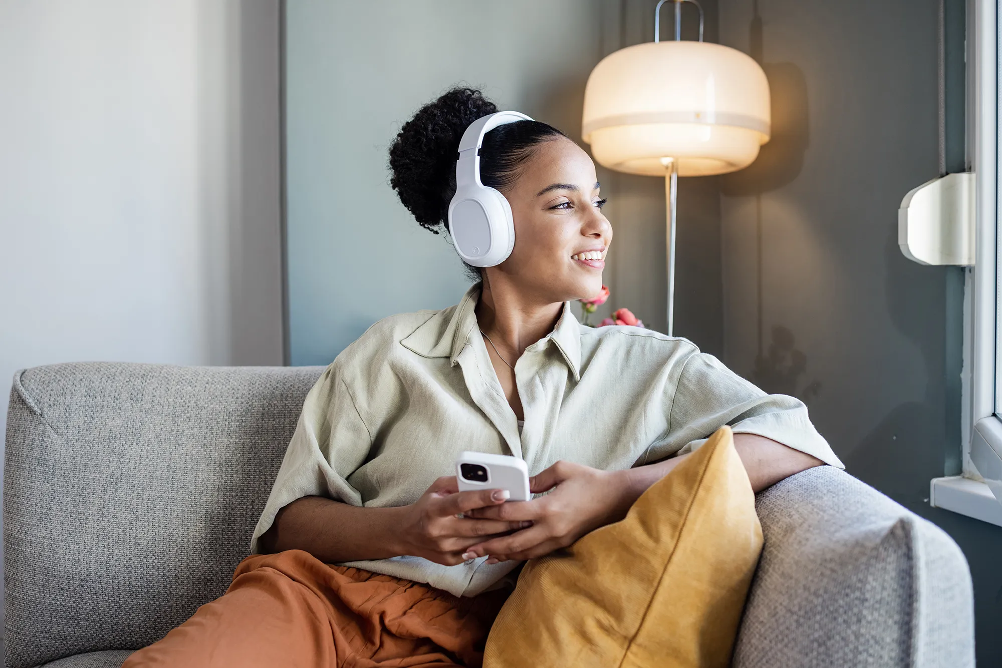 Young African American woman with wireless headphones relaxing on the couch and listening her favourite music on smart phone
