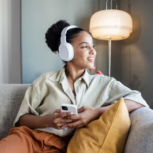 Young African American woman with wireless headphones relaxing on the couch and listening her favourite music on smart phone