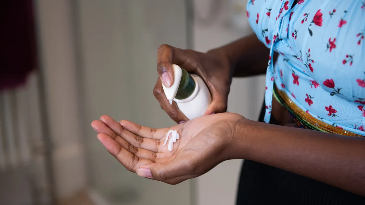 Young woman moisturising her hands and arm with cream in a domestic bathroom