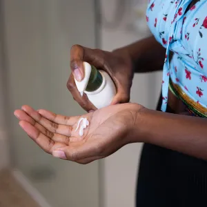 Young woman moisturising her hands and arm with cream in a domestic bathroom