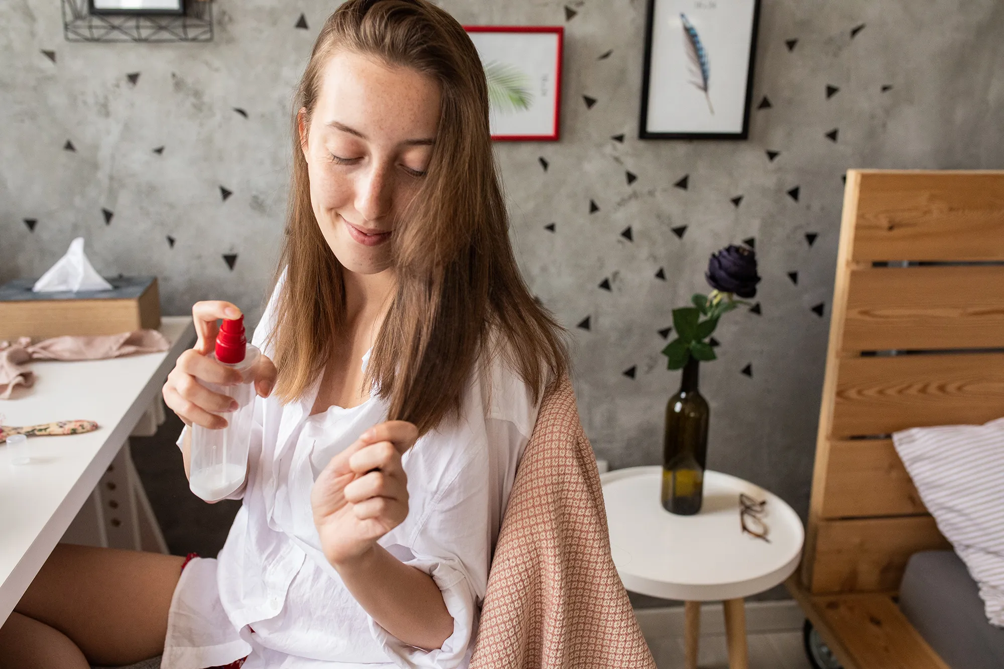 Young woman using hair spray in bedroom early in the morning