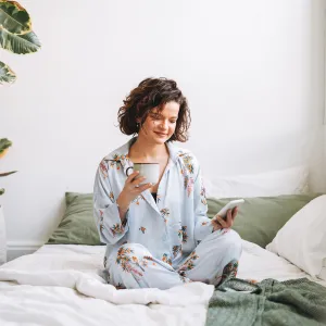 Young brunette woman with curly hair in pajamas using mobile on bed at home