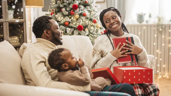 Young family unwrapping gifts on Christmas morning. Mother is getting cookbook.
