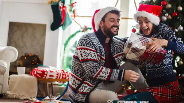 Copy space shot of jolly young couple sitting on the floor in their living room under Christmas and having excited looks on their faces after opening gifts.