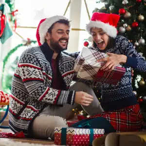 Copy space shot of jolly young couple sitting on the floor in their living room under Christmas and having excited looks on their faces after opening gifts.