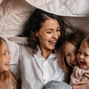 Happy mother with three girls holding blanket on sofa at home